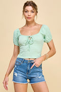 Woman wearing a light green top and denim shorts on a beige background