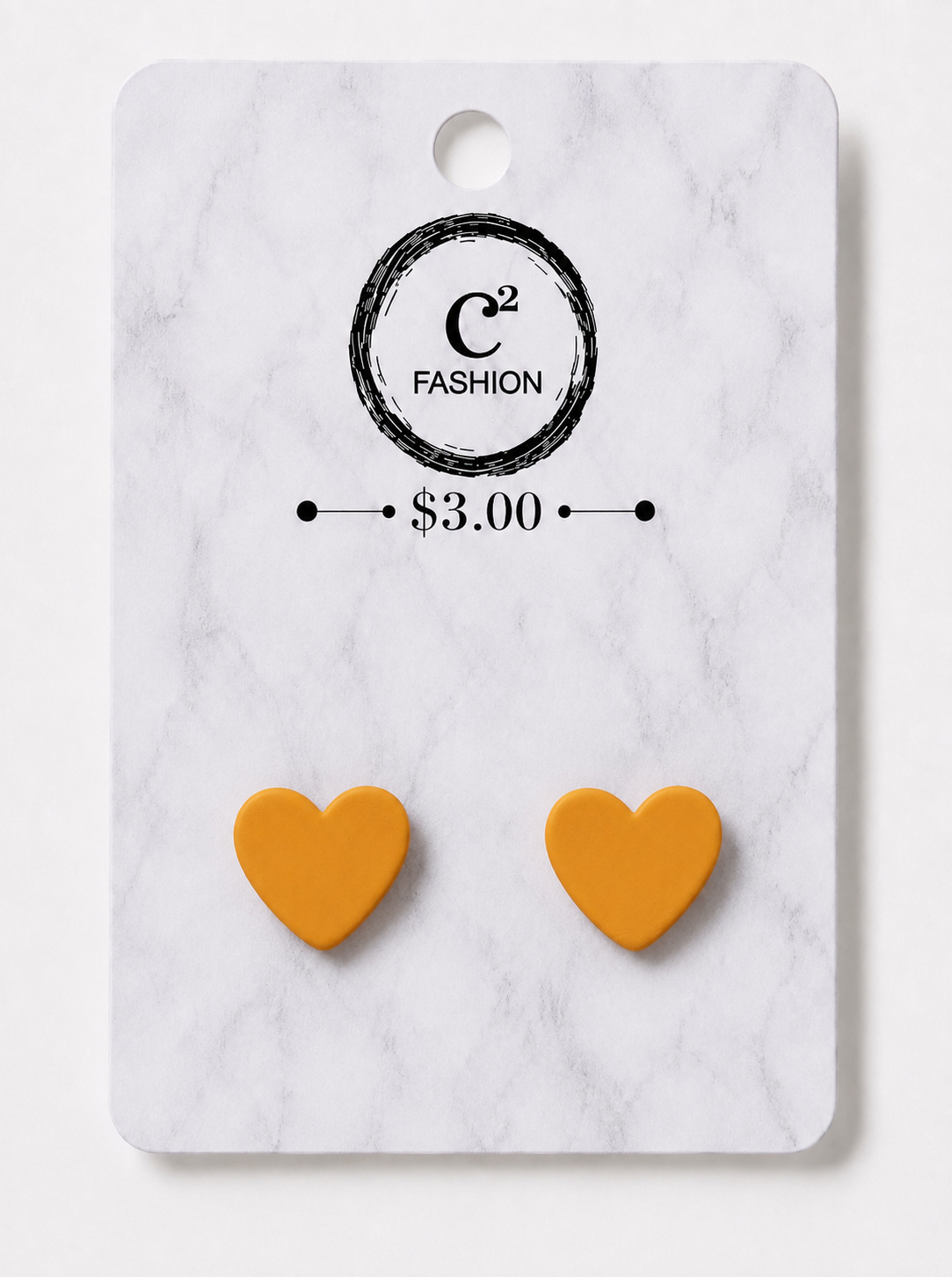 A pair of small heart-shaped yellow-orange stud earrings displayed on a white marble-patterned retail card with the C2 FASHION logo and $3.00 price printed above them.
