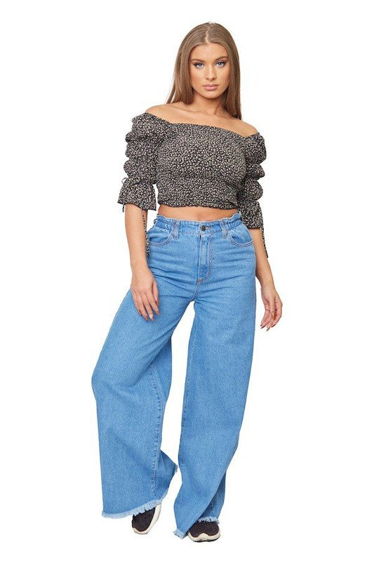 Woman wearing a patterned off-shoulder top and blue jeans on a white background
