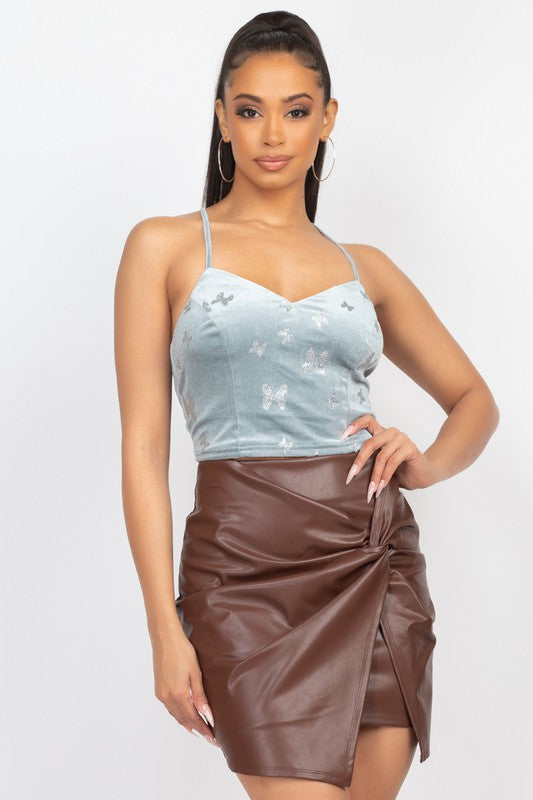 Woman wearing a light blue top with butterfly design and a brown leather skirt on a white background