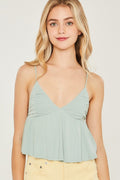 Woman wearing a light green top with thin straps on a plain background