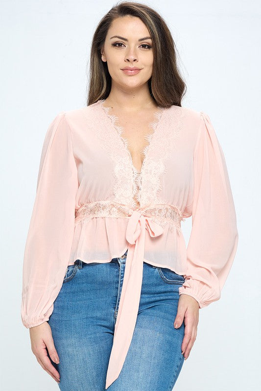 Woman wearing a light pink blouse with lace details and blue jeans on a white background