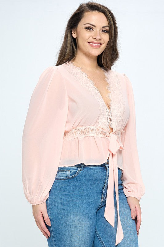 Woman wearing a light pink blouse with a lace detail and blue jeans on a white background