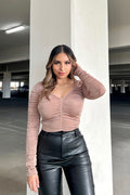 Woman wearing a pink long-sleeve top and black leather pants in an indoor setting.