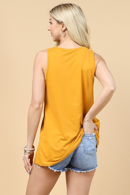 Woman wearing a mustard yellow sleeveless top and denim shorts on a beige background