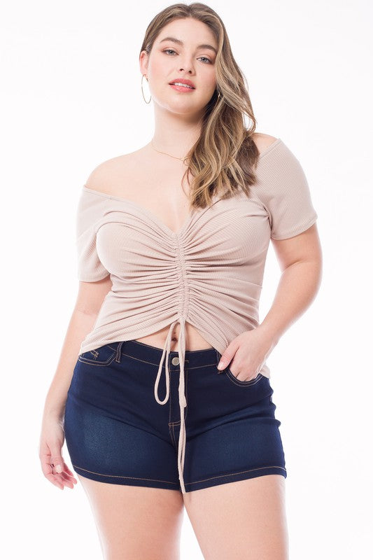Woman wearing a beige ruched top and dark blue shorts on a white background