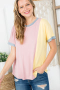 Woman wearing a pink and yellow color-blocked shirt with blue jeans indoors.