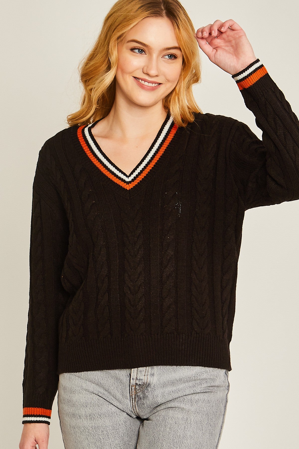 Woman wearing a black sweater with orange and white trim on a plain background