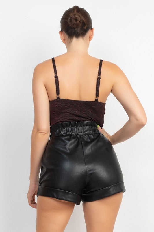 Person wearing a brown top and black leather shorts on a white background