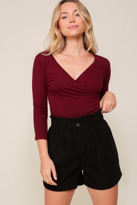 Woman wearing a burgundy top and black shorts against a beige background