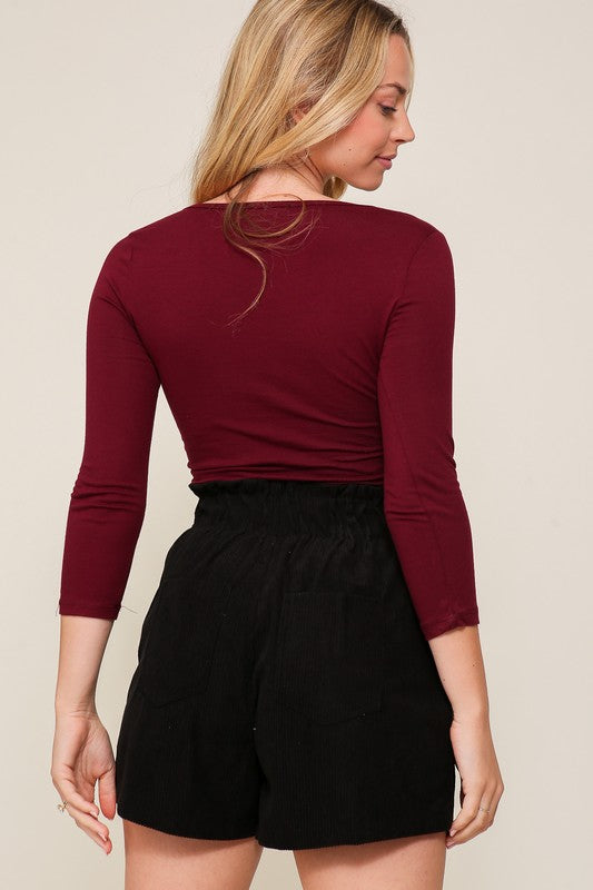 Woman wearing a burgundy long-sleeve top and black shorts on a beige background