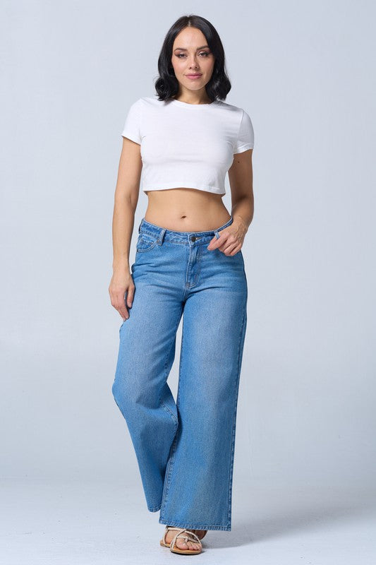 Woman wearing a white crop top and blue flared jeans on a light gray background