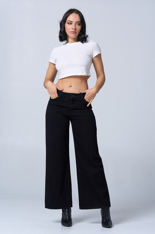 Woman wearing a white crop top and black wide-leg pants on a light gray background
