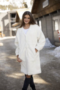Woman wearing a white coat standing outdoors with snow and a building in the background
