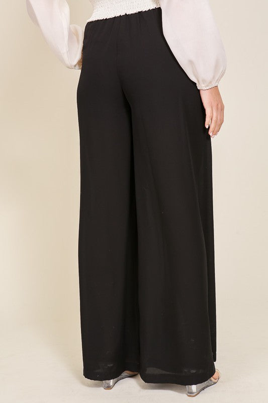 Black wide-leg pants worn with a white blouse on a beige background