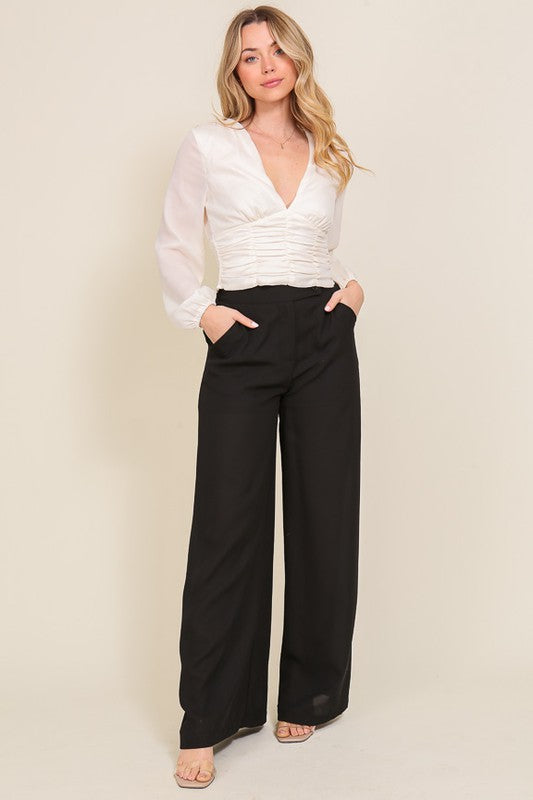 Woman wearing a white blouse and black pants against a beige background