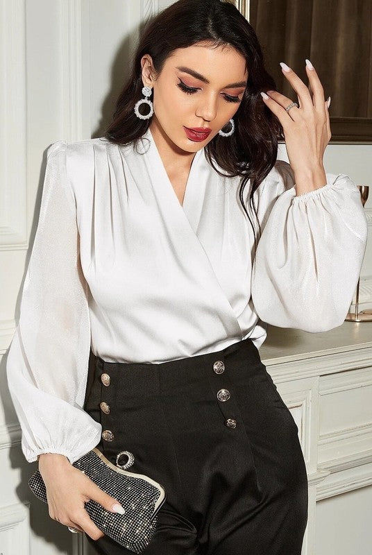 Woman wearing a white blouse with puffed sleeves and black high-waisted pants, holding a clutch.