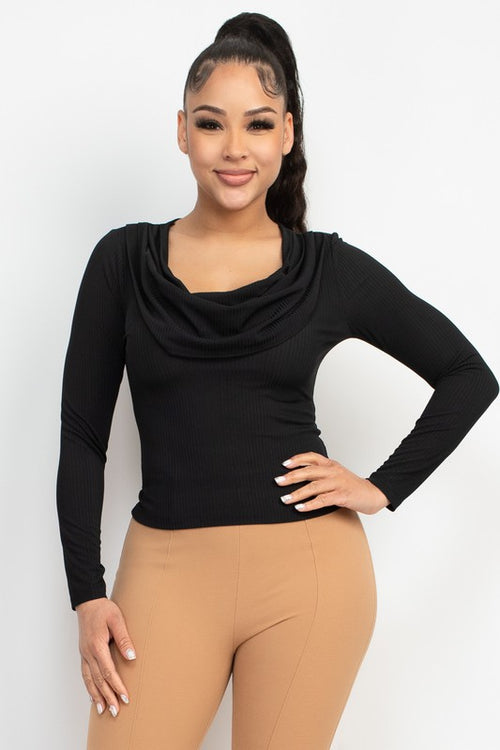 A woman modeling a black long-sleeve cowl neck top paired with tan leggings, standing against a plain light gray studio background.