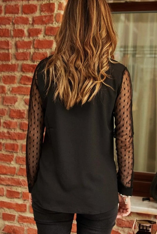 Person wearing a black sleeveless top with sheer sleeves against a brick wall.