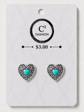 A pair of heart-shaped stud earrings with silver filigree borders and turquoise centers, mounted on a white display card printed with the brand name 'C2 FASHION' and a price of '$3.00'.