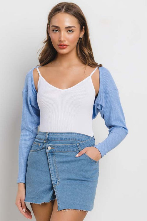 Woman wearing a blue cardigan, white top, and denim skirt against a plain background