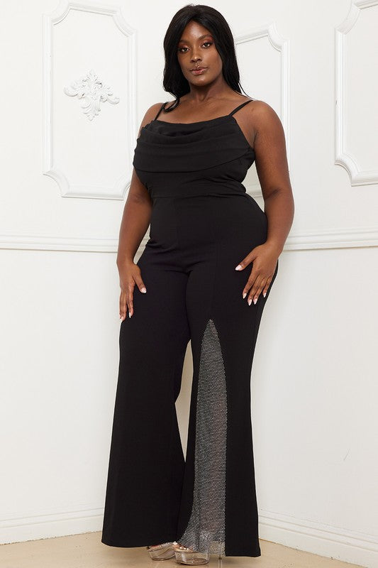 Woman wearing a black jumpsuit with sheer side panels against a white wall.