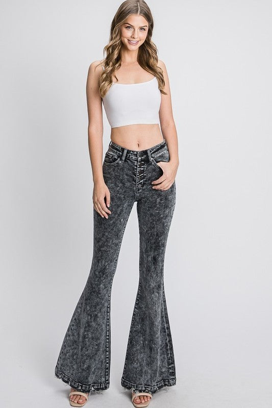 Woman wearing a white top and black acid-wash flared jeans on a light gray background
