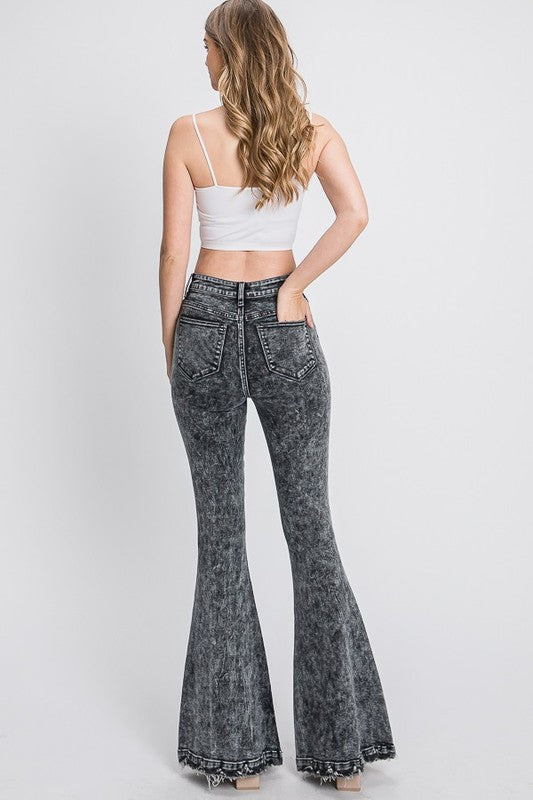 Woman wearing acid-wash flared jeans and a white top on a plain background