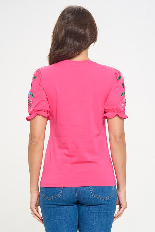 Person wearing a pink t-shirt with floral designs on the sleeves against a white background
