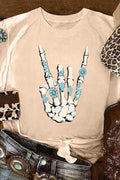 Beige t-shirt with a skeleton hand design featuring blue flowers, surrounded by cowboy boots and a belt.
