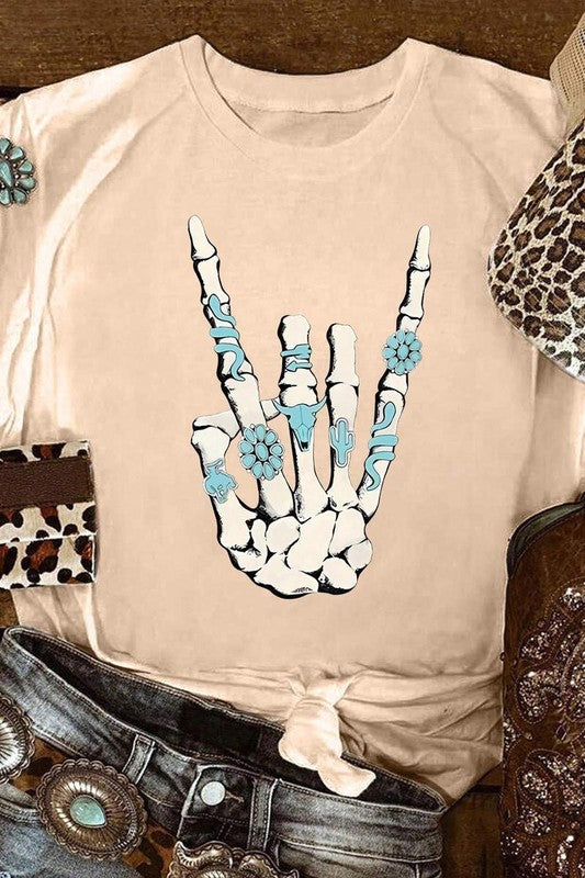 Beige t-shirt with a skeleton hand design featuring blue flowers, surrounded by cowboy boots and a belt.