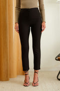 Person wearing black pants and a beige top in a room with wooden paneling.