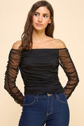 Woman wearing a black off-shoulder top with sheer sleeves on a beige background