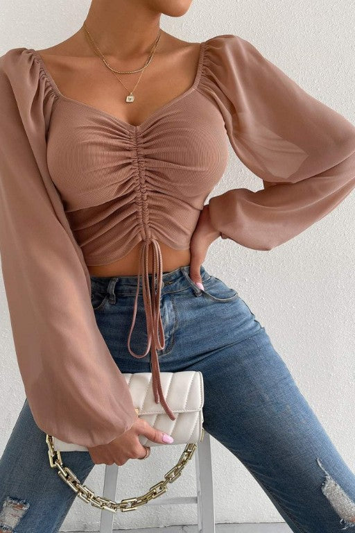 Woman wearing a brown ruched top and blue jeans, holding a beige handbag.