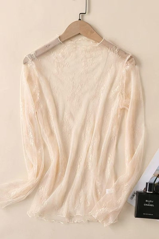Sheer beige lace top on a hanger with a magazine and perfume bottle in the background.