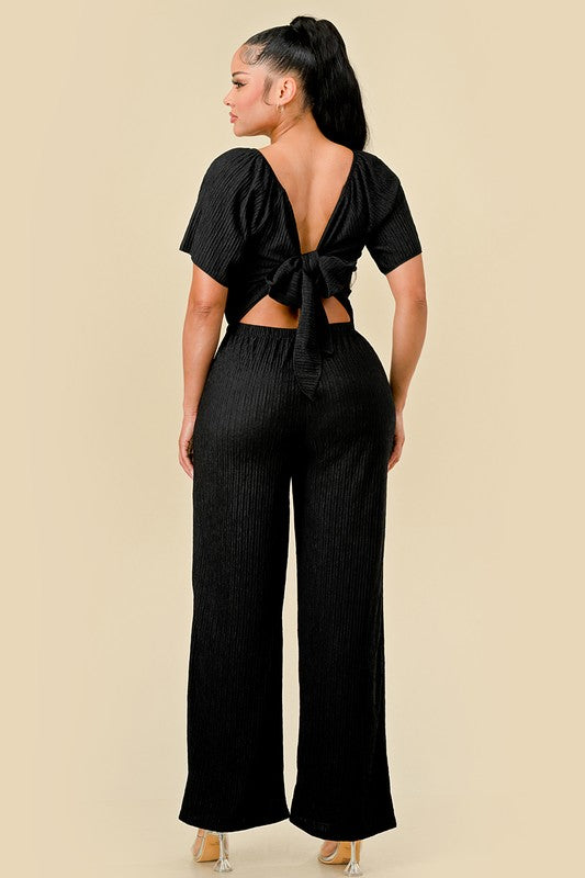 Woman wearing a black open-back top and wide-leg pants on a beige background