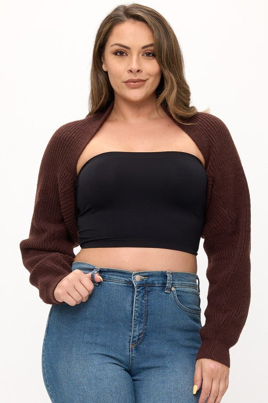 Woman wearing a brown cardigan, black tube top, and blue jeans on a white background