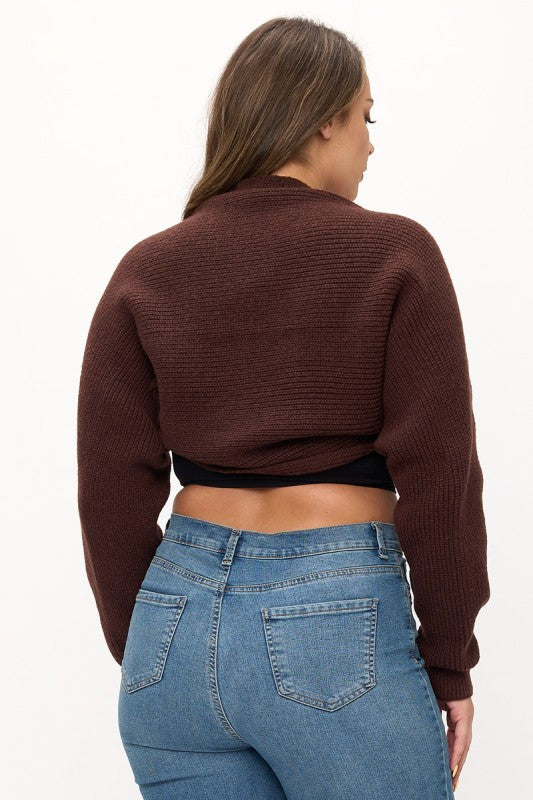 Person wearing a brown cropped sweater and blue jeans on a white background