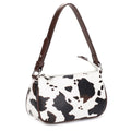 Handbag with cow print pattern on a white background with brown handle. 
