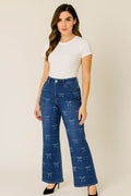 Woman wearing blue jeans with bow pattern and a white top on a beige background