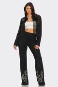 Woman wearing a black fringe jacket and black pants with white patterns on a white background