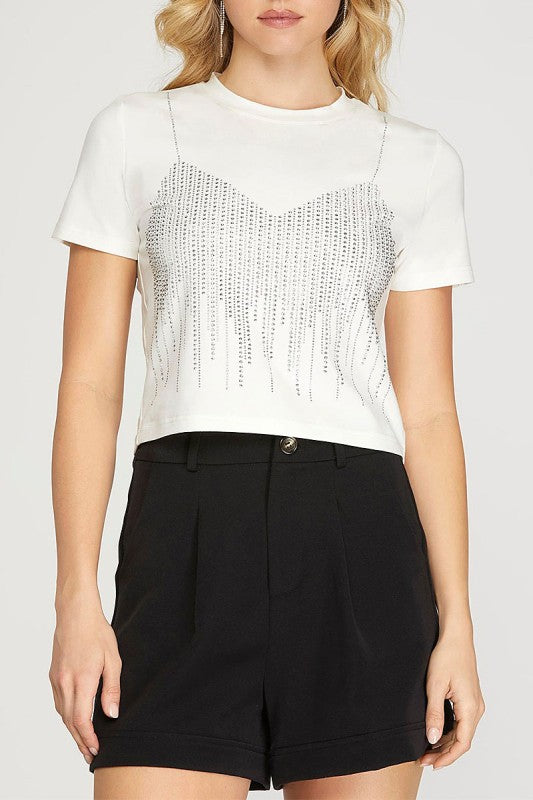 Person wearing a white t-shirt with beaded details and black shorts on a plain background