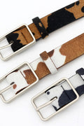 Three Cow print belts with a silver buckle on a white background