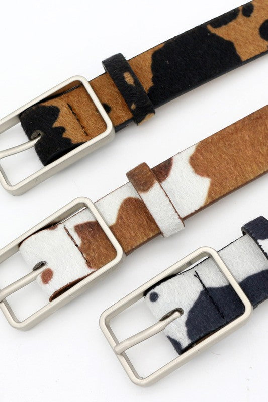 Three Cow print belts with a silver buckle on a white background