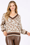 A woman modeling a beige and brown leopard-print knit sweater with a V-neck and brown faux-leather pants against a plain white background.