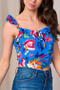 Woman wearing a colorful floral top with blue jeans against a neutral background