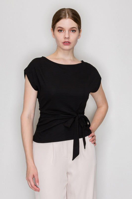 Woman wearing a black top with a tie detail on a plain background