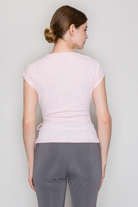 Woman wearing a light pink top and gray pants against a plain background