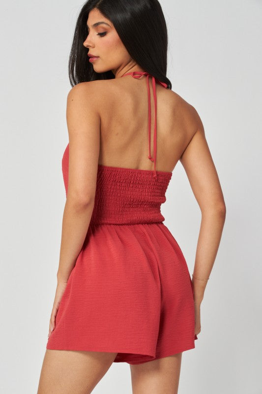 Woman wearing a red halter neck romper against a plain background