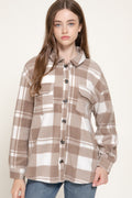 Model wearing an oversized taupe and cream plaid shacket with button closure and two chest pockets, paired with blue jeans.
